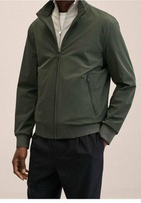 Ciemnozielona kurtka z wysokim kołnierzem, z przodu na zamek błyskawiczny, z bocznymi kieszeniami i ściągaczami przy mankietach. Gładki materiał z dopasowanym krojem.