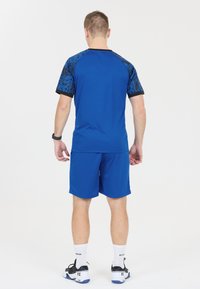 Blå idrottströja och shorts med ett svart mönsterdesign på axlarna. Tillverkad av lättviktig och andningsbar tyg. Svarta accenter på ärmarna.