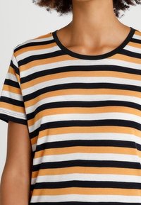 Pruhované tričko s horizontálními černými, bílými a hořčicovými pruhy, kulatým výstřihem s černým lemem, krátkými rukávy a měkkou tkaninou.