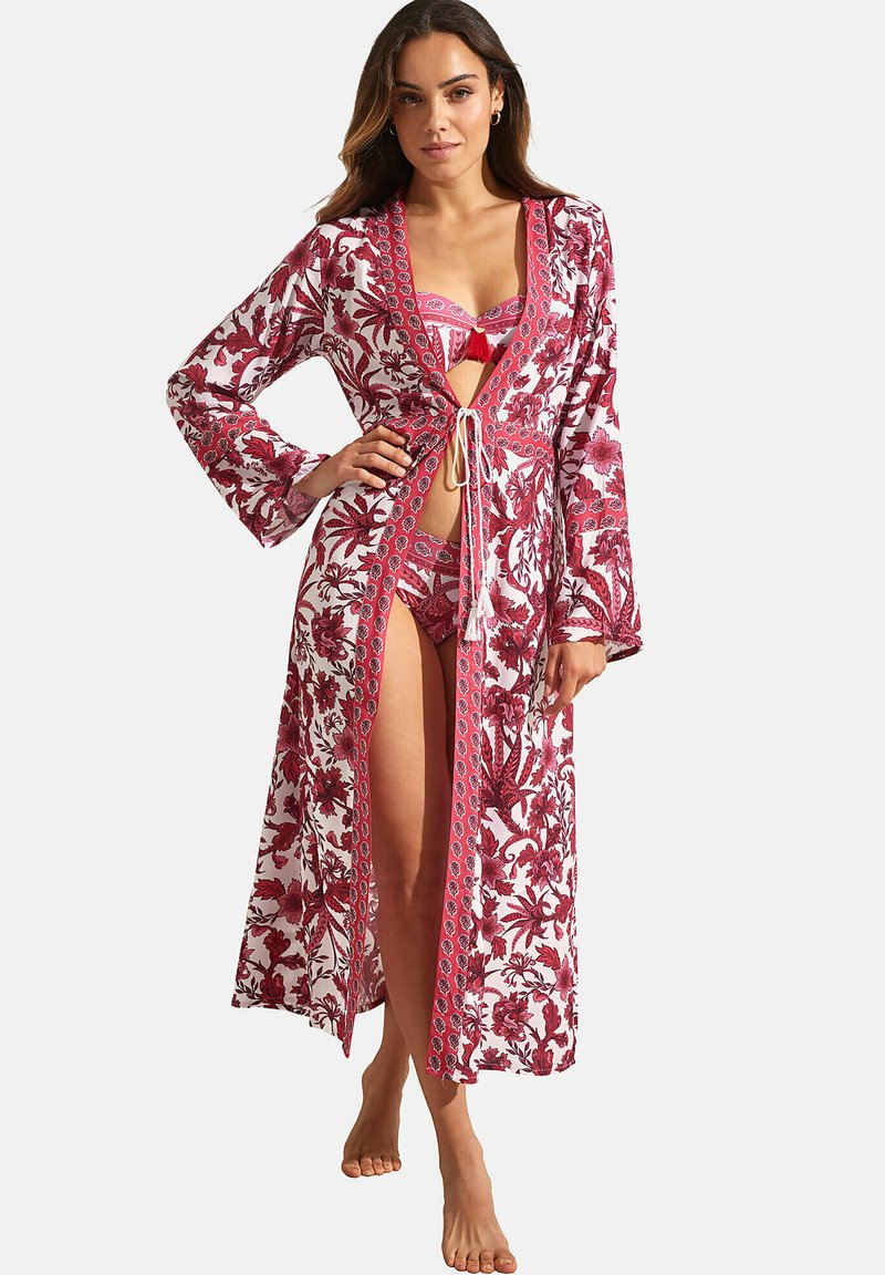 Lange, lichte gewaad in het wit met rode bloemenpatronen. Heeft een strik in de taille en brede mouwen. Eronder een bijpassende bikini-set.