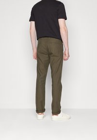 Oliwkowe chinosy o prostym kroju, z podwiniętymi nogawkami i standardowym pasem. Połączone z czarnym t-shirtem i białymi trampkami.
