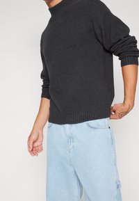 Maglione grigio scuro lavorato a maglia con scollo rotondo a coste e maniche con polsini, abbinato a jeans di denim azzurro chiaro con tasca laterale.