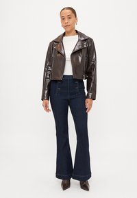 Jaqueta de moto em imitação de couro castanho com fecho prateado, design curto, combinada com jeans flare de um azul escuro com detalhes em botão.
