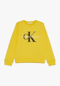 Sudadera de cuello redondo amarilla con el logotipo en blanco y negro de "Calvin Klein Jeans" centrado en el pecho, y puños y dobladillo de canalé.