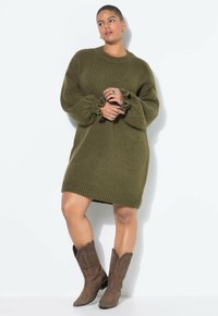 Übergroßes, olivgrünes Strickkleid mit gerippten Bündchen und Saum, kombiniert mit braunen Cowboystiefeln. Strukturierter Stoffabschluss.