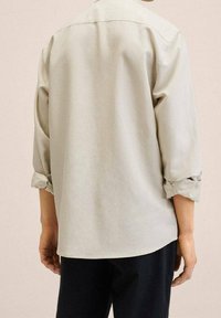 Camicia grigia chiaro con una vestibilità rilassata e maniche arrotolate, realizzata in un tessuto morbido con una consistenza liscia e un design pulito e sottile.
