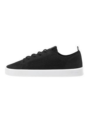Sort strikket lav-top sneaker med sorte snørebånd og hvid gummisål, der viser sideprofil med træksløjfe ved hælen.