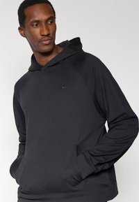 Sudadera negra de Nike con bolsillo canguro, mangas raglán y un logo sutil en el pecho, con un acabado liso y texturizado.