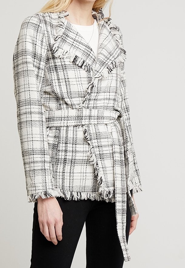Veste portefeuille à carreaux noir et blanc, avec des bords effilochés, une ceinture à nouer et un col à revers. Confectionnée dans un tissu texturé avec une coupe structurée.