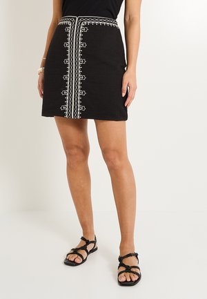 Falda negra con bordado blanco en el centro, que cuenta con una tela texturizada, una forma ajustada y una cinturilla con costuras decorativas.