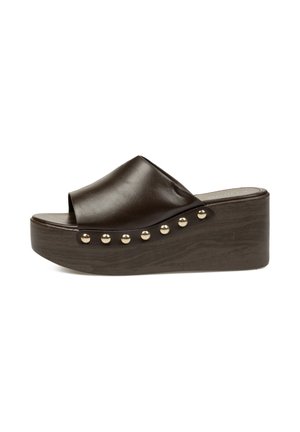 Sandalia tipo slide de cuero marrón oscuro con cuña de plataforma y tachuelas de tono dorado a lo largo del borde de la suela.