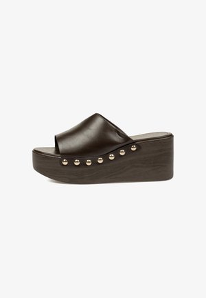 Sandalia tipo slide de cuero marrón oscuro con cuña de plataforma y tachuelas de tono dorado a lo largo del borde de la suela.