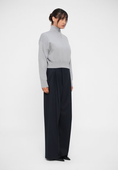 Pulover scurt, cu fermoar, de culoare gri, asortat cu pantaloni evazați, cu talie înaltă, de culoare bleumarin. Texturi fine, design minimalist și detalii subtile cu plissare.