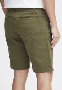 Olivgröna stretchshorts med slät front, elastisk midja och bakfickor. Tyget är mjukt med en avslappnad passform och längd ovanför knäna.