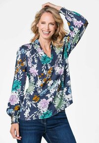 Blumenbluse mit navy Hintergrund, die lebendige Blumen in Grün, Lila und Orange zeigt. Lange Ärmel, V-Ausschnitt und geraffte Details.