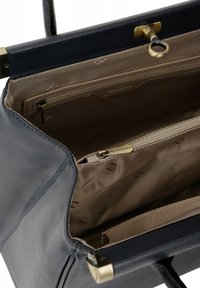 Granatowa skórzana torebka o strukturalnym kształcie, z wewnętrzną kieszonką na zamek i beżowym podszyciem. Mosiężne okucia podkreślają design.
