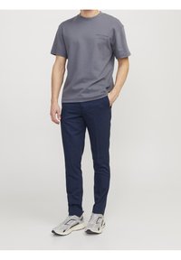 Grå bomullströja med korta ärmar och tryckt design, kombinerad med marinblå byxor och grå sneakers med mesh- och gummisulor.