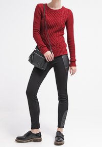 Röd stickad tröja med kabelmönster, svarta tajta byxor med läderdetaljer, och svarta skor. Crossbody-väska med en stilren design.