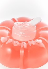 Maschera notte Abib PDRN collagen in gel trasparente, contenuta in un barattolo rotondo rosa, posizionata su un anello gonfiabile corallo luminoso con lettere.
