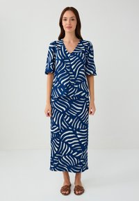 Completo due pezzi blu navy composto da una maglietta a maniche corte e una gonna lunga con un motivo a foglie bianche. Tessuto intrecciato, vestibilità comoda. Sandali marroni.