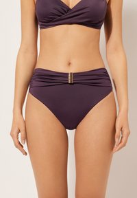 Lila bikiniuppsättning med en omslagstopp och högmidjade bottnar. Bottnarna har en texturerad guldfinish vid midjan.