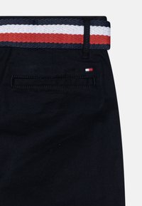 Černá látka s tkaným barevným páskem, který má červené, bílé a námořnické pruhy. Detaily zadní kapsy se malým vyšitým logem.