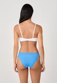 Bikini bottom a righe blu con una forma alta, abbinato a un top bandeau bianco con spalline regolabili e chiusura con gancio.