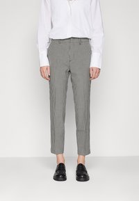 Grå och vit rutiga byxor med smal passform, kort längd och subtil textur, i kombination med svarta slip-on skor.