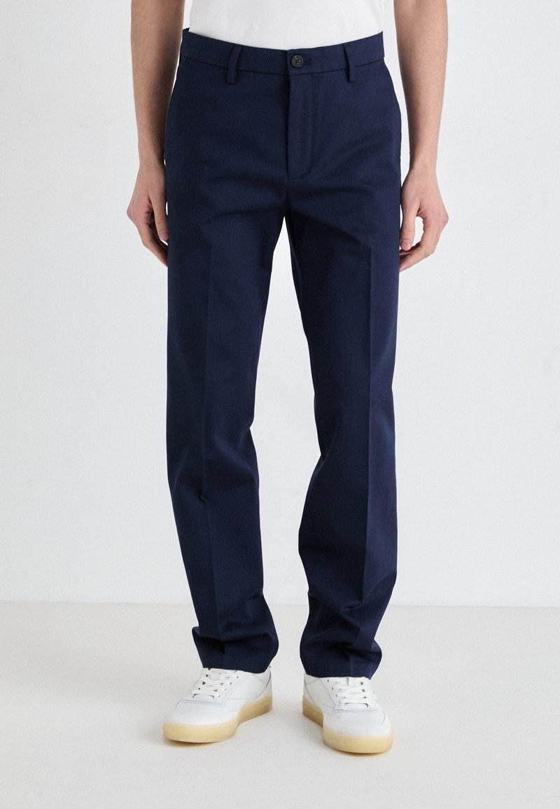 Navy blue trousers with a straight fit, crafted from smooth fabric, featuring a single button closure and side pockets. Worn with white sneakers.