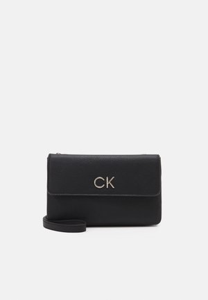 Pochette en cuir noir Calvin Klein avec fermeture à rabat et logo métallique CK sur le devant, présentée sur un fond clair uni.