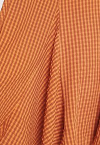Raidallinen kangas lämpimissä oranssin ja ruskean sävyissä, jossa on ryppyinen pinta ja vuorotellen paksuja ja ohuita viivoja. Pehmeä ja kevyt kangas.