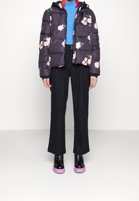 Černá prošívaná bunda s květinovým potiskem, modrý žebrovaný svetr, černé kalhoty s širokými nohavicemi a černé boty s fialovými platformními podrážkami.