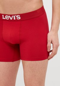 Röda bomullsboxerbriefs med en vit Levi's-logga på midjebandet, med en figursydd design, mjuk textur och minimala sömnadsdetaljer.