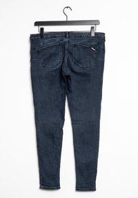 Pantalones vaqueros skinny azul oscuro con una textura suave, cinco bolsillos y detalles de costura sutiles, presentados colgados de un gancho negro.