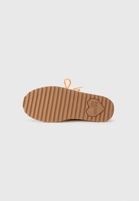 Suela de zapato de goma con una textura ondulada, presenta un logo en forma de corazón grabado, y cordones naranjas enhebrados a través de agujeros.