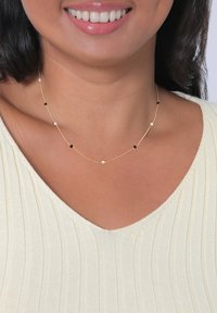 Collana d'oro con piccole perle nere e bianche, design della catena delicato, appoggiata su un top a scollo a V, minimalista ed elegante.