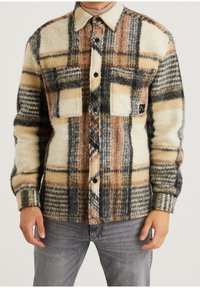 Koszula flanelowa w kratę w odcieniach beżu, pomarańczy i czerni. Posiada dwie kieszenie piersiowe, zapięcie na guziki oraz teksturowane wykończenie. Dopasowany krój.