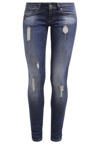 Jean skinny en denim bleu foncé, avec des patchs déchirés et des détails effilochés. Conception classique à cinq poches avec fermeture éclair et bouton.