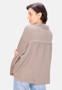 Helle beige, strukturierte Overshirt mit Kragen, lockerer Passform und Falten am Rücken. Kombiniert mit hellblauen Jeans.