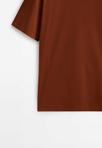T-shirt marron uni à manches courtes avec coutures visibles sur la manche et l'ourlet, présenté sur un fond blanc.