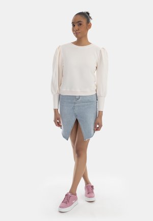 Felpa rosa chiaro con maniche a sbuffo, abbinata a una gonna in denim blu con spacchetto frontale. Indossata con sneakers rosa.
