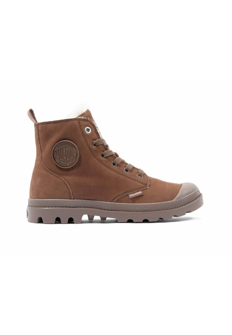 Ruskea nahkainen nilkkuri, jossa on pyöreä kärki, valkoinen turkisvuori, kumipohja, jossa on uritukset, ja pyöreä logo sivussa.