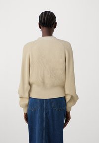 Beige ribbestrikket genser med rund hals og ballongsleeves, kombinert med et denimskjørt med to baklommer.