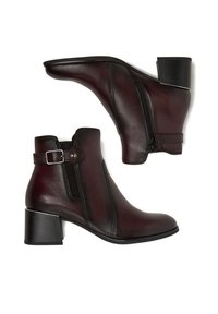 Tumepruuni nahast pahkluu saabastega, külgse lukuga, kontrastsete elastsete paneelidega, dekoratiivse pandlaga ja massiivse kontsaga. Sile tekstuur ja lihtne disain.