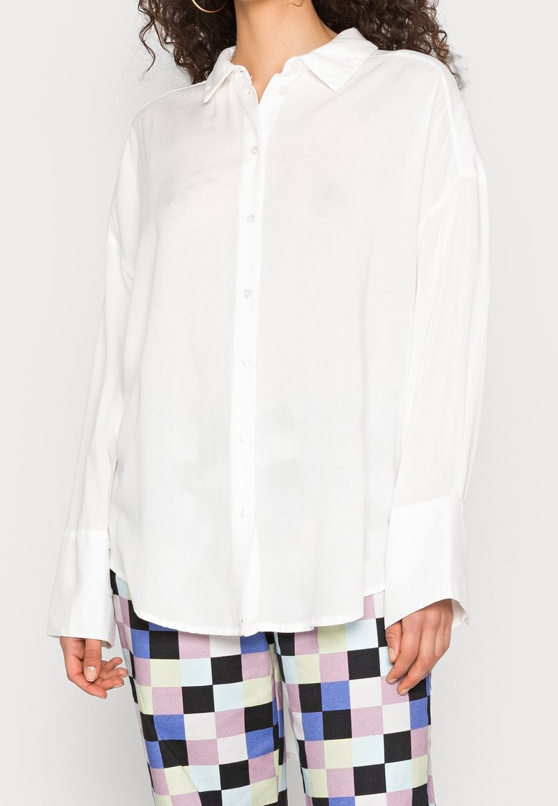 Vit skjorta med knappar i ett mjukt, lättviktigt tyg, med en klassisk krage och långa ärmar som smalnar av vid ärmsluten.