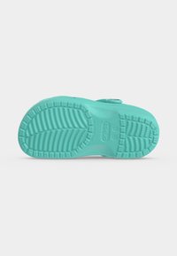 Σόλα μιας τιρκουάζ σαγιονάρας Crocs που δείχνει δομημένο σχέδιο πέλματος και ενδείξεις μεγέθους σε απλό ανοιχτό φόντο.