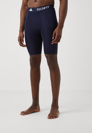 Navy compression shorts made of stretchy fabric, featuring a white Adidas Techfit logo on the waistband and a fitted design.