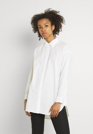 White button-up shirt with a collared neck, long sleeves, and a slightly longer back hem, made from a smooth cotton blend fabric.