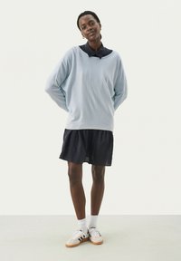 Helles blaues übergroßes Sweatshirt mit einem marineblauen Hemd darunter, kombiniert mit einem dunklen Rock und weißen Schuhen mit schwarzen Streifen.