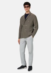 Olivgrüne, gerippte Doppelreiherjacke mit zwei Fronttaschen, kombiniert mit hellgrauen Hosen und schwarzen Sneakers. Modell trägt dunkle Sonnenbrillen.